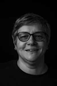 Eine Frau mit Brille und Nasenpiercing lächelt freundlich