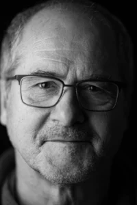 Portraitfoto eines älteren Mannes mit ernstem Blick und Brille in schwarz weiss