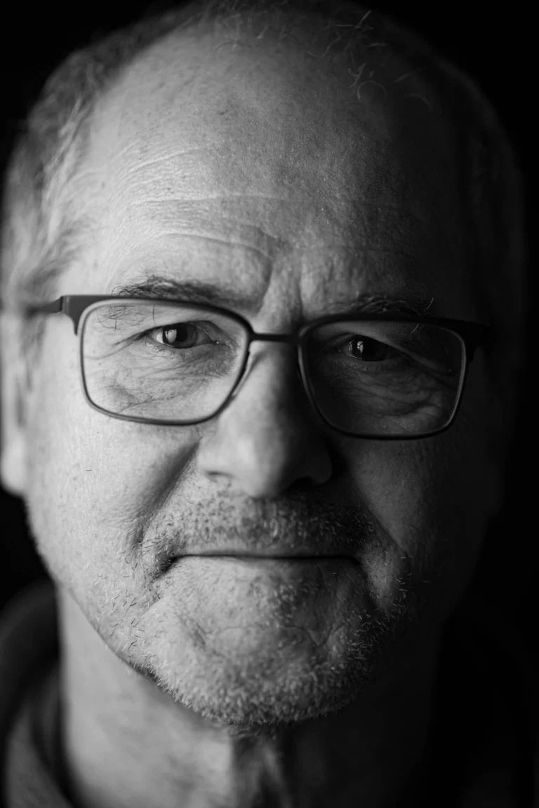 Portraitfoto eines älteren Mannes mit ernstem Blick und Brille in schwarz weiss